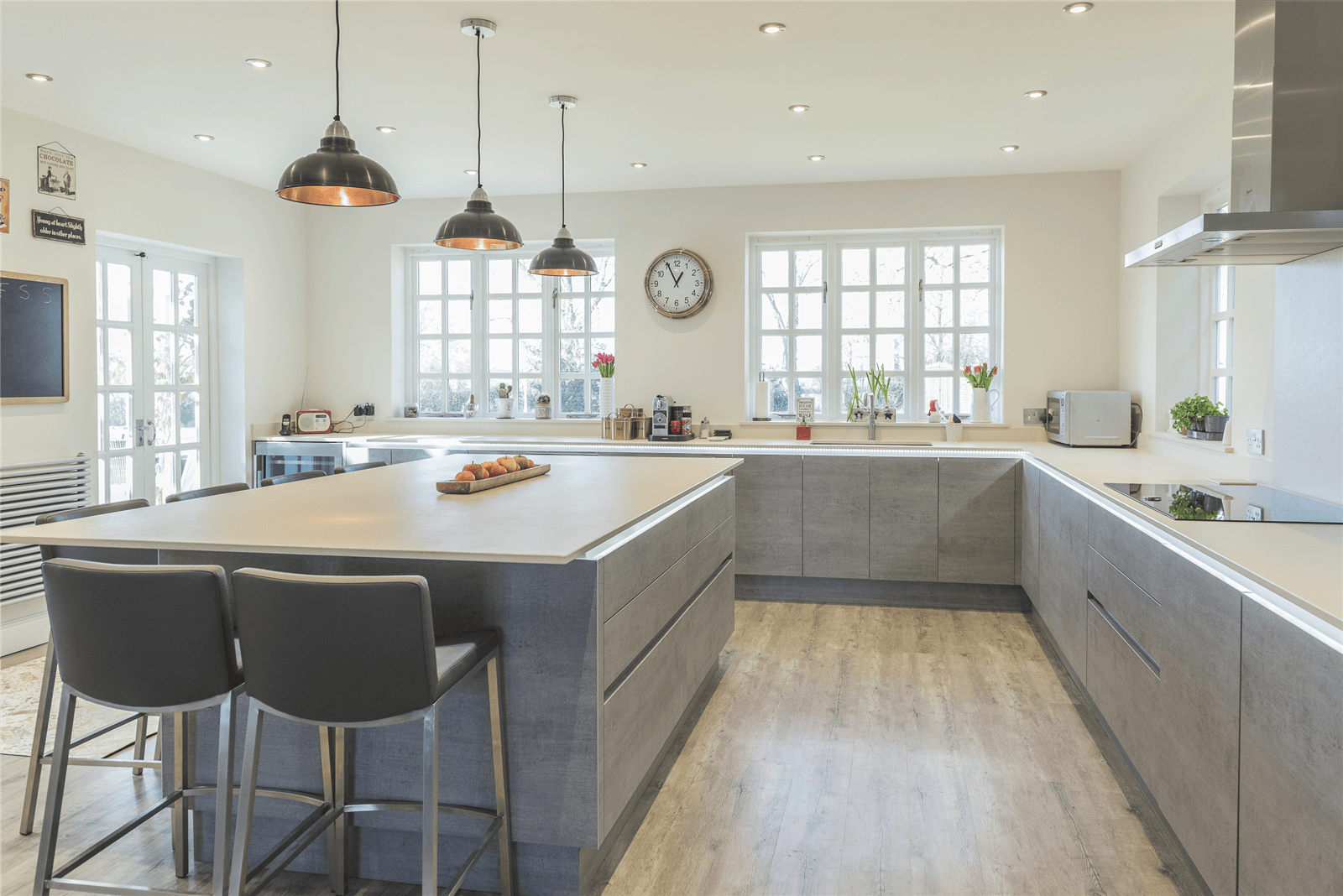 Bespoke fitted kitchen in Liverpool featuring a large central island with breakfast bar seating, painted handleless cabinets, pendant lighting, and oak-effect flooring.