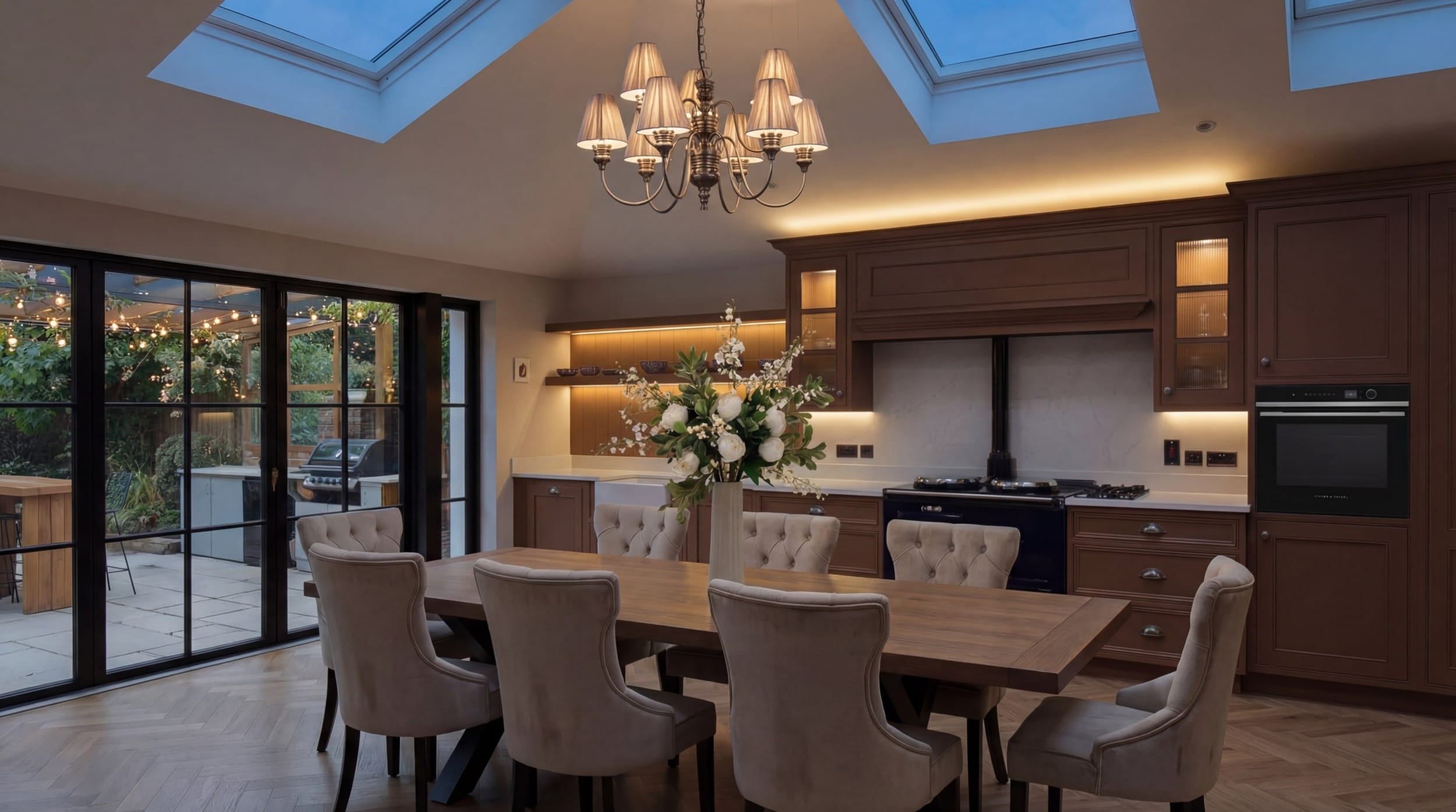 Mastercraft bespoke kitchen with warm timber cabinetry, range cooker alcove, quartz worktops and skylit dining area opening to the garden through black steel framed doors.