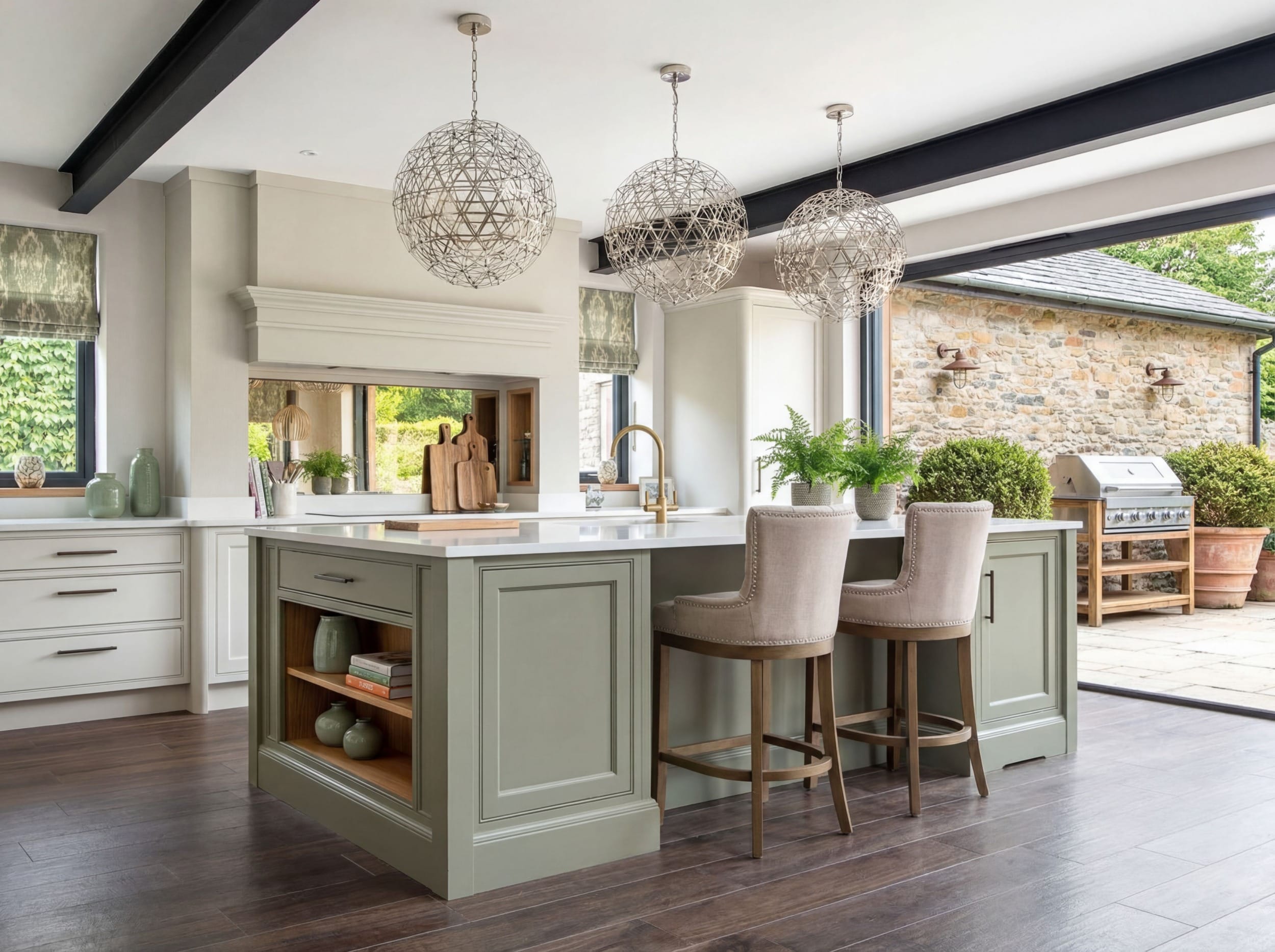 harrogate kitchen 3 Bespoke painted shaker kitchen in a Yorkshire home featuring a large central island with seating, white quartz worktops, brass tap, open shelving, and three sculptural pendant lights beneath exposed ceiling beams, with wide sliding doors opening onto a stone patio.
